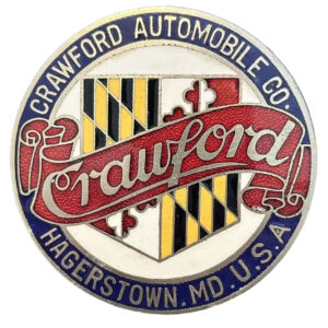 Colorful circular, metal emblem this is 2.25” diameter. Red banner with silver “Crawford” in script across middle, over a multi-color badge. White background in middle, blue edge with “Crawford Automobile Co., Hagerstown, MD, USA” on it.