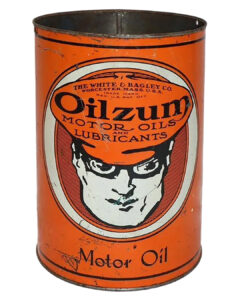 Oilzum Metal 5 Quart Oil Can. Orange can with some wear and discoloration. “THE WHITE & BAGLEY CO” and “WORCESTER, MASS. USE” is written in tiny black letters on the top. “OILZUM MOTOR OILS & LUBRICANTS” is written in large black letters below in the center followed by a white and black goggle-eyed man graphic. “Motor Oil” is written in small black letters on the bottom.