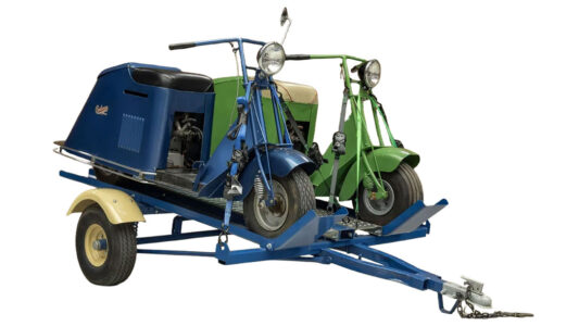 Matching Pair of 1947 Cushman Model 47 Motor Scooters w/ Custom Hosclaw Trailer. One scooter is bright green, the other a metallic bright blue. Trailer is matching blue.
